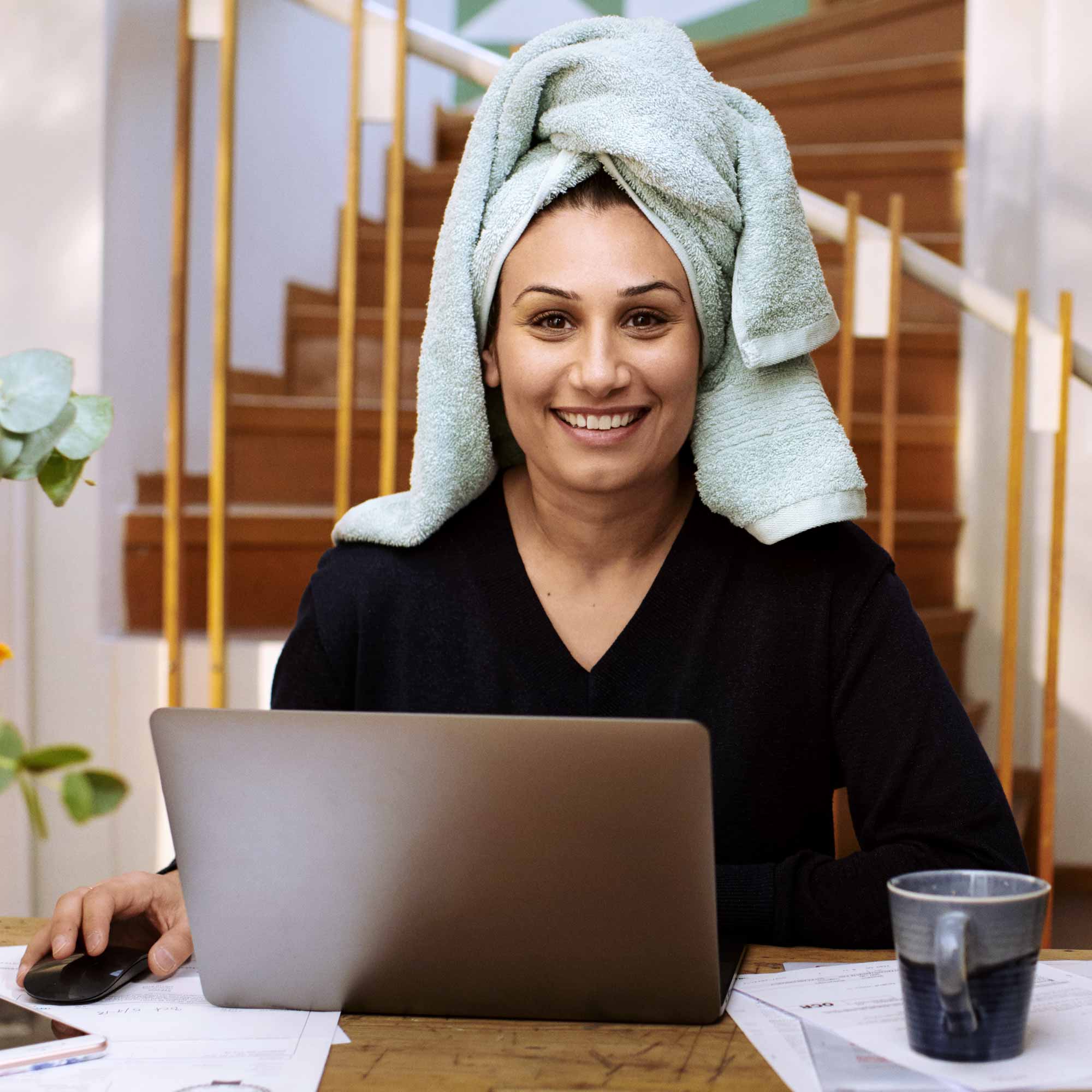 Glad kvinna med en blå handuk om håret sitter hemma framför en dator