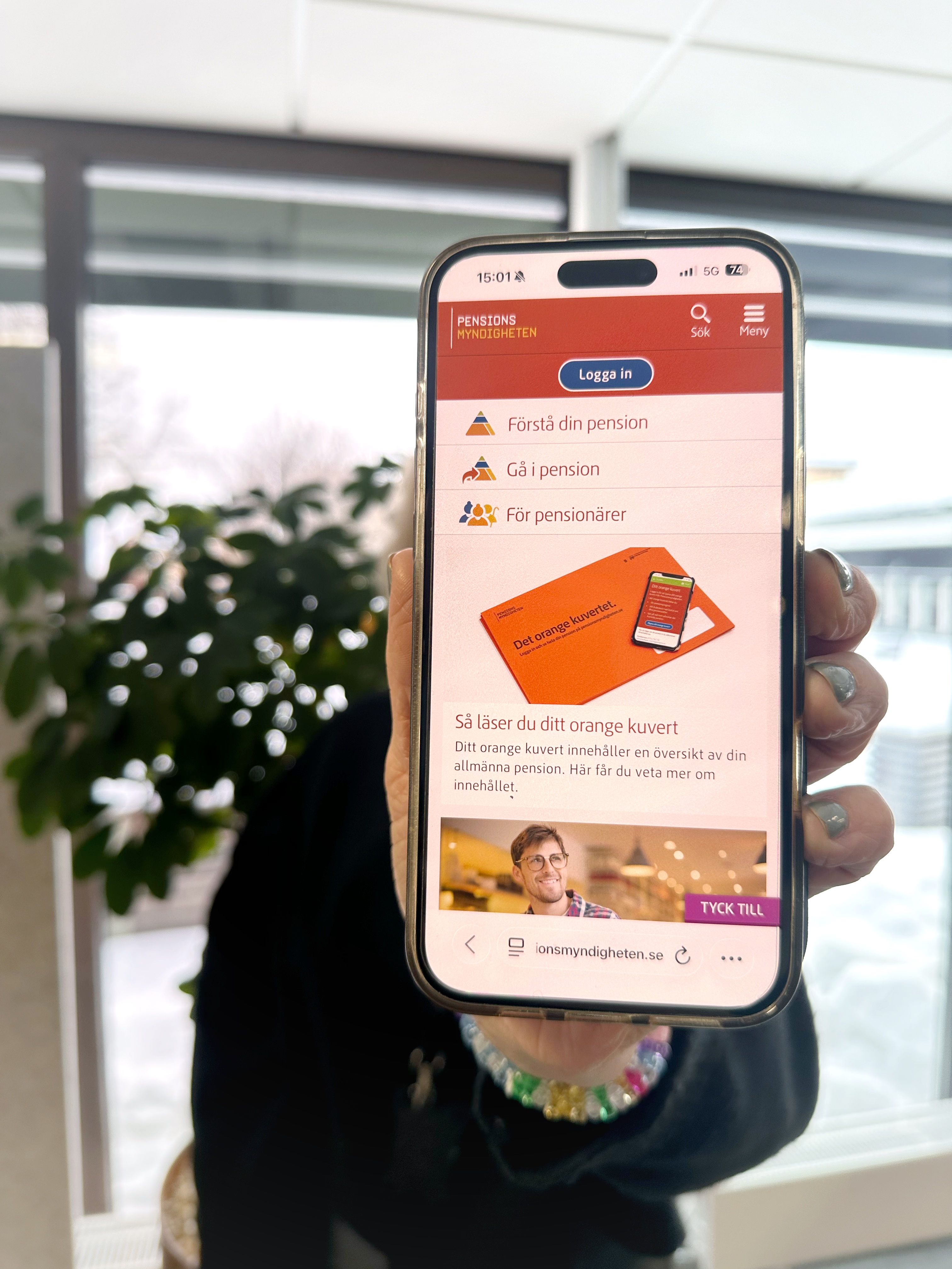 Person som håller i mobiltelefon där skärmen visar Pensionsmyndighetens startsida.